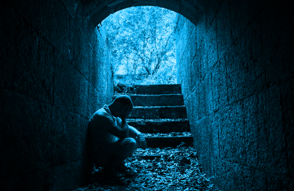 Support for victims of domestic abuse. Solitary figure in contemplative pose inside a serene stone tunnel leading to an inviting natural escape.